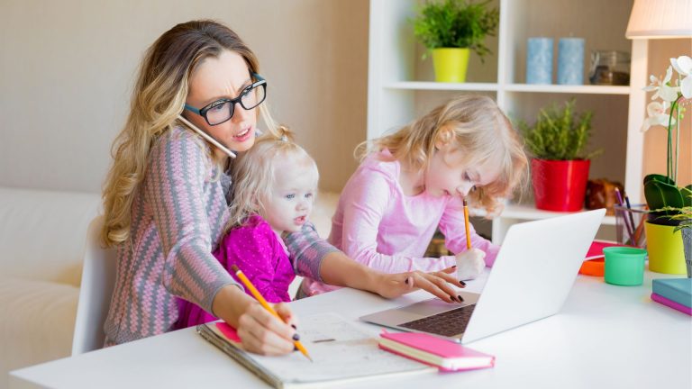 Mutter sitzt mit Laptop, To-do-Liste und Kaffee am Küchentisch – Symbol für Mütter als Managerinnen des Alltags.